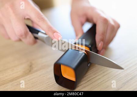 Woman sharpens knife with sharpener in kitchen close-up. Stock Photo