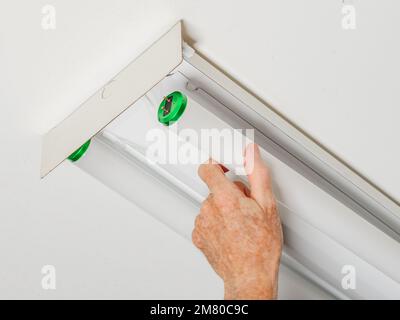 Electrician changing fluorescent light bulb in ceiling light fixture. Man replacing burned out fluorescent light tube. Stock Photo