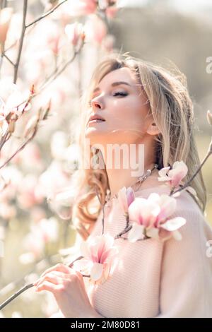 Portrait of a beautiful happy middle aged woman enjoying the smell in a blooming spring garden. Beautiful magnolia bushes, large flowers. Stock Photo