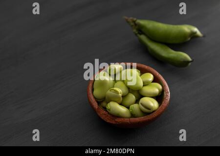 freshly peeled green beans in a clay bowl with a bunch of broad beans to the side, with copy space. Stock Photo