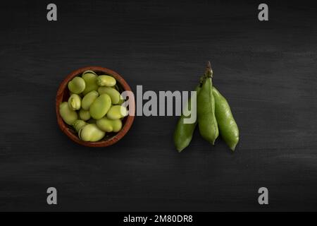 freshly peeled green beans in a clay bowl with a bunch of broad beans to the side, with copy space. Stock Photo