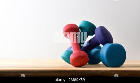 Background with dumbbells of different weights and colors on a wooden base and white isolated background. Front view. Stock Photo