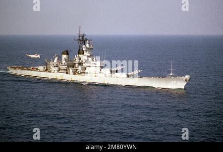 A starboard view of the battleship USS NEW JERSEY (BB-62) underway with a Helicopter Anti-submarine Squadron 5 (HS-5) SH-3H Sea King helicopter hovering over the stern. Country: Mediterranean Sea (MED) Stock Photo