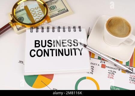 Business concept. On the table is a cup of coffee, money, business charts and a notepad with the inscription - Business Continuity Stock Photo