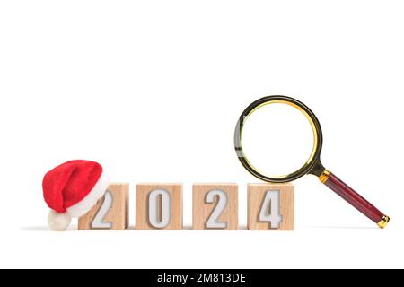 Wooden cubes with numbers 2024 with Santa hat and magnifying glass on white background Stock Photo