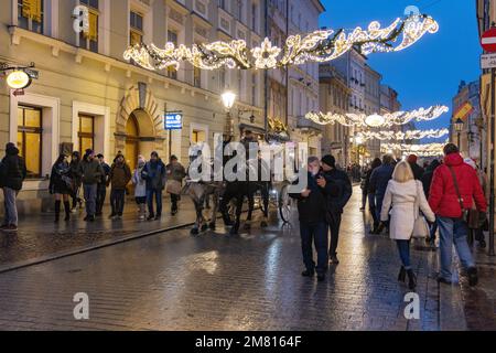 Krakow Street scene; local people tourists and a horse and carriage on Grodzka street on a winter evening at Christmas, Krakow Old Town, Krakow Poland Stock Photo