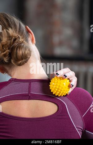 The athlete does a relaxing massage of the neck and back with the help of a prickly rubber ball. Stock Photo