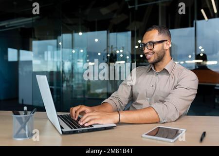Young successful Indian programmer working inside modern development company, man using laptop to write code for software. Stock Photo