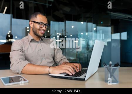 Young successful Indian programmer working inside modern development company, man using laptop to write code for software. Stock Photo