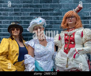 Portrait of three women, female steampunks, smiling while standing next to a wall. Dressed in period costume, steampunk clothing. Stock Photo