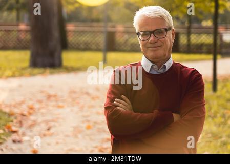 Portrait of grey-haired man pensioner with folded arms in the park. High quality photo Stock Photo
