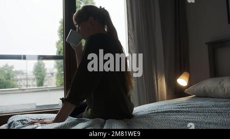 back view of a woman on a bed drinking hot coffee and relaxing, cozy mood. High quality photo Stock Photo
