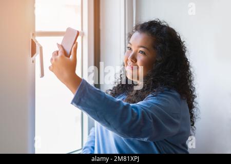 portrait beautiful chubby latin young woman taking selfies with a mobile phone indoors. Stock Photo