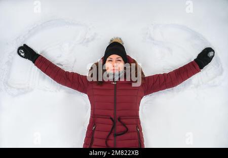 Top view of woman in red winter coat making snow angel on winter day. Stock Photo