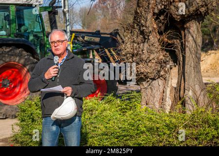 A man announces the imminent felling of the village lime tree in Borschemich near Erkelenz, North Rhine-Westphalia, Germany, speaking into a microphone with notes in hand. Behind him, a tractor fitted with a grapple arm already waits, while the 329-year-old tree still stands untouched. On 27 February 2016, former residents fell the tree themselves, because they do not want to have this symbol of their identity taken away from them as well – the village's last landmark after the demolition of its church and Haus Paland. The village made way for the Garzweiler opencast lignite mine. Its resident Stock Photo