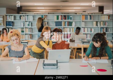 Multiethnic male and female students taking notes and using laptops in library Stock Photo