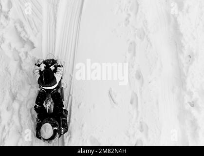 Aerial overhead done photo of two children in a sled going down a snow covered hill.  Stock Photo