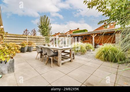 an outdoor patio with table, chairs and potted plants in the background is a blue sky filled with white clouds Stock Photo