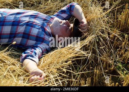Senior farmer in the hay. Senior taking a break and relaxing on a hay on an summer day. Grandfather laying on haystack in countryside. Mature man Stock Photo