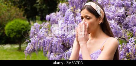 Spring allergy, flu. Banner. Girl with nose allergy sneezing. Polen illnes symptom concept. Woman allergic to blossom during spring blooming tree Stock Photo