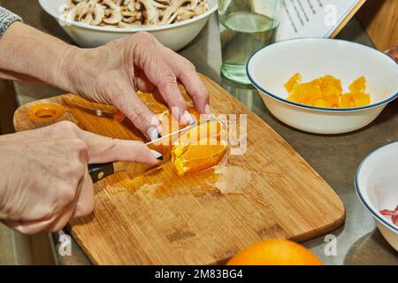 Chef cuts oranges to prepare salad with zucchini, oranges and salami. French gourmet cuisine, on a wooden background. Stock Photo