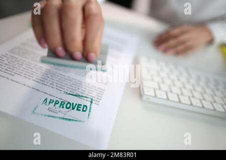 Closeup of a person hand stamping green approved seal on text approved document on table Stock Photo