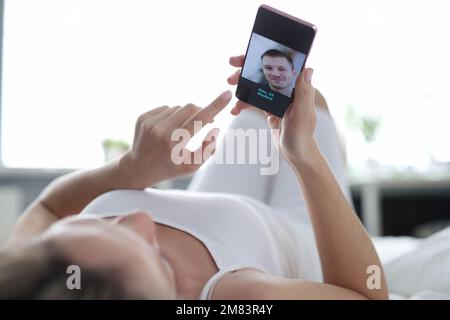 Young woman looking through profiles of men on dating app on mobile phone Stock Photo