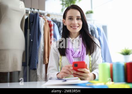 Young seamstress designer at workplace in atelier holds smartphone Stock Photo