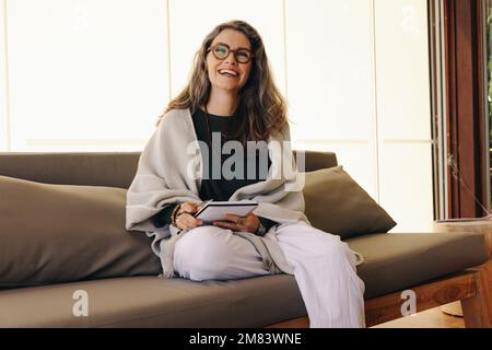Journaling and mental wellbeing. Mature woman smiling happily while writing and entry in her diary at home. Cheerful senior woman writing down her emo Stock Photo