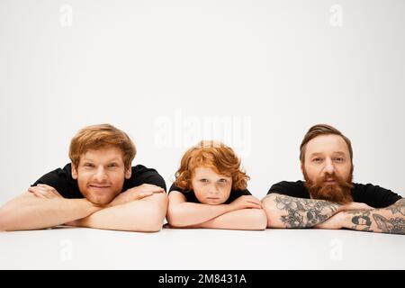 cheerful man with redhead son and bearded tattooed father lying with crossed arms on light grey background,stock image Stock Photo