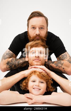 family portrait of bearded tattooed man with red haired son and grandson on light grey background,stock image Stock Photo