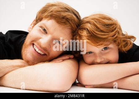 family portrait of redhead father and son lying with crossed arms and smiling at camera on light grey background,stock image Stock Photo