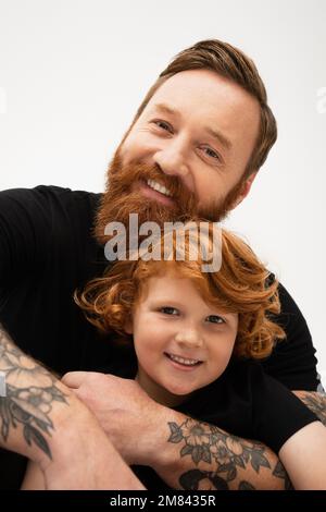 family portrait of red haired boy with bearded tattooed grandpa smiling at camera isolated on grey,stock image Stock Photo