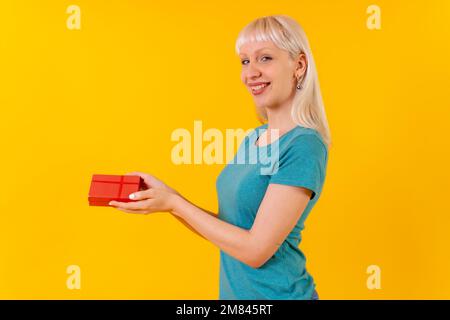 A blonde Caucasian woman holding a surprise gift on the yellow background Stock Photo