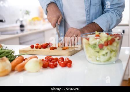 Close up of man at home preparing vegetables salad for lunch. People in the kitchen cooking and enjoying healthy food lifestyle. One unrecognizable ma Stock Photo