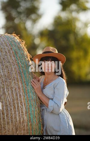 A beautiful middle-aged woman without makeup with well-groomed skin and silky hair poses near a haystack Stock Photo