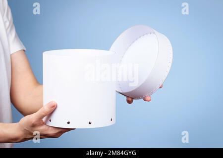 Woman hands holding white round cardboard box and open cap on light blue background. Mock up package box Stock Photo