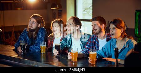 Friends, young people, men and women watching match at pub. Fans emotionally watching sport competition Stock Photo