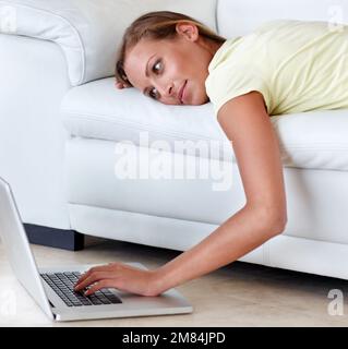 Relaxing browsing. A young woman lying on her couch with her hand resting on her laptops keyboard. Stock Photo