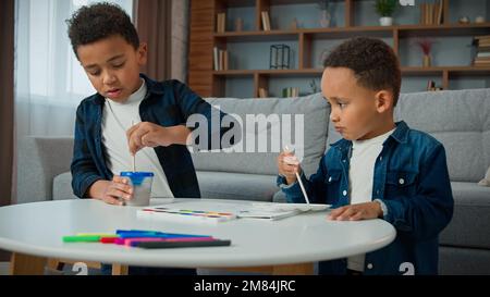 Two brothers African American children kids ethnic sons sibling painting at home together with acrylic watercolor colors little boys schoolboys Stock Photo