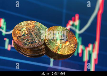 Two heaps of golden bitcoins on blue digital background with cryptocurrency chart indicating plummeting of price with red candlestick going down Stock Photo