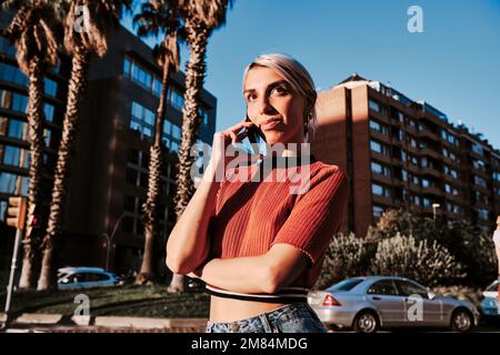Woman looking away while talking on the phone standing outdoors. Stock Photo