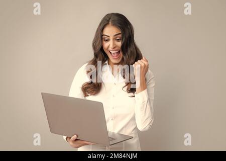 Portrait of a cheerful young casual girl standing isolated over gray background, using laptop computer. Business woman at work. Stock Photo