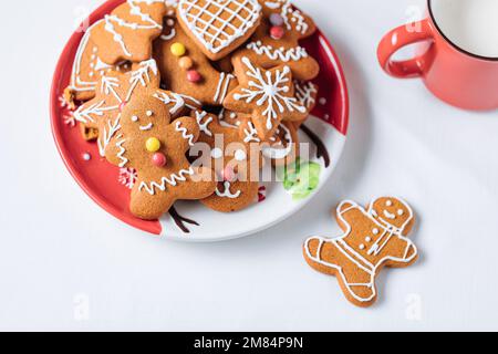 Gingerbread cookies in shape of ginger man placed on red plate. White background. Traditional Christmas dessert decorated. Playful and happy. Stock Photo