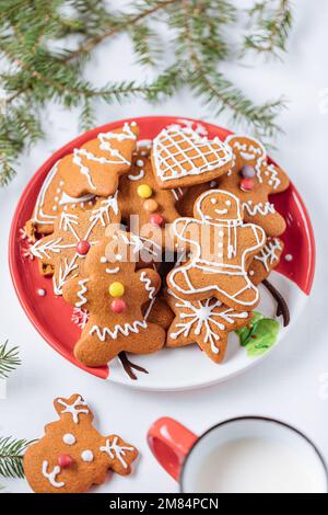 Gingerbread cookies in shape of ginger man placed on red plate. White background. Traditional Christmas dessert decorated. Playful and happy. Stock Photo