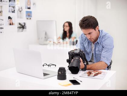 Using the tools of the trade. Two photographers sitting in their office working on layouts and inspecting their equipment. Stock Photo