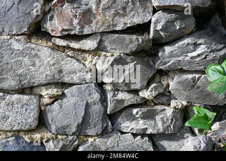 Rough dry-stacked stone wall with irregular grey rocks, creating a rustic masonry texture and traditional construction background Stock Photo
