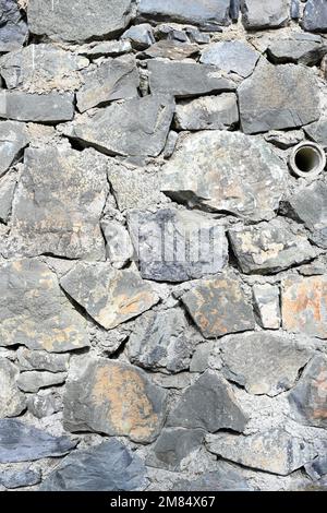 Rough dry-stacked stone wall with irregular grey rocks, creating a rustic masonry texture and traditional construction background Stock Photo