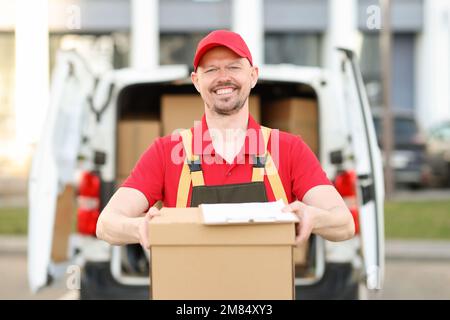 Smiling courier stands in front of van with parcel Stock Photo