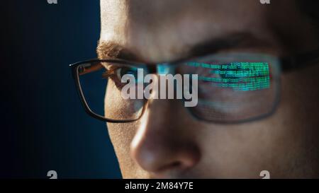 Close-up portrait of focused software engineer wearing eyeglasses looking at computer screen working with big data. Programming code reflecting in glasses. Data science, Machine Learning, AI concept Stock Photo